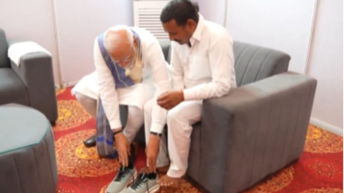 பிரதமர் நரேந்திர மோடி பரிசளித்த ஸ்னீக்கர்களை ராம்பால் காஷ்யப் அணிய உதவுகிறார். | X/@narendramodi
