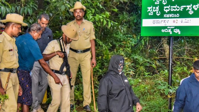 கர்நாடகாவின் தட்சிண கன்னட மாவட்டத்தில் உள்ள தர்மஸ்தலத்தில் திங்கள்கிழமை (கருப்பு நிற உடையில்) தகவல் தெரிவித்த நபருடன் பாதுகாப்புப் பணியாளர்கள் | PTI
